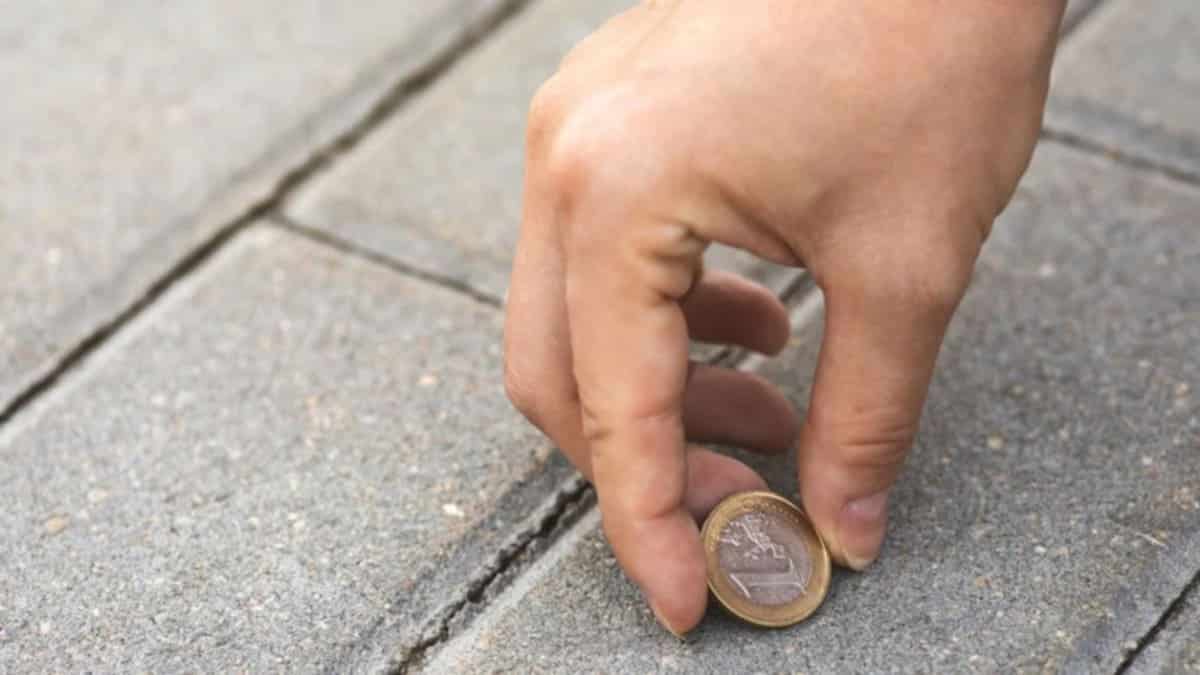 Une main ramassant une pièce de monnaie sur un sol pavé