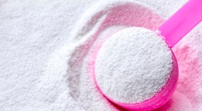 Cuillère doseuse au-dessus d'un paquet de lessive en poudre