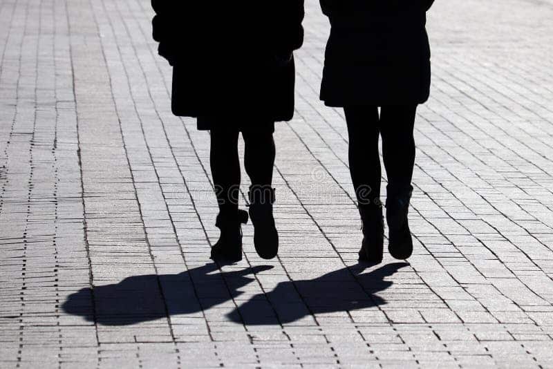 Silhouettes de deux femmes marchant côte à côte dans une rue en pente